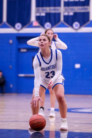 Basketball player in white Braintree uniform crouches in defensive stance on blue court during game.