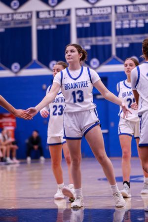 Basketball players in white uniforms perform defensive drill on blue court during practice.