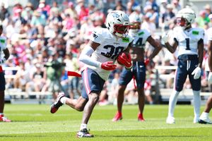 Football player in white jersey runs with ball during sunny outdoor game.