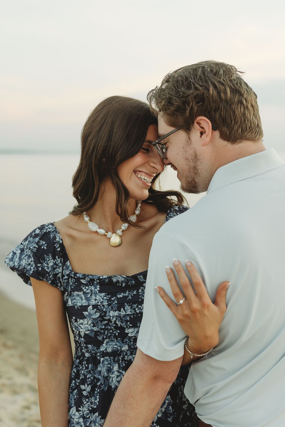Couple sharing a romantic moment on the beach, woman in floral dress laughing as man leans in close.