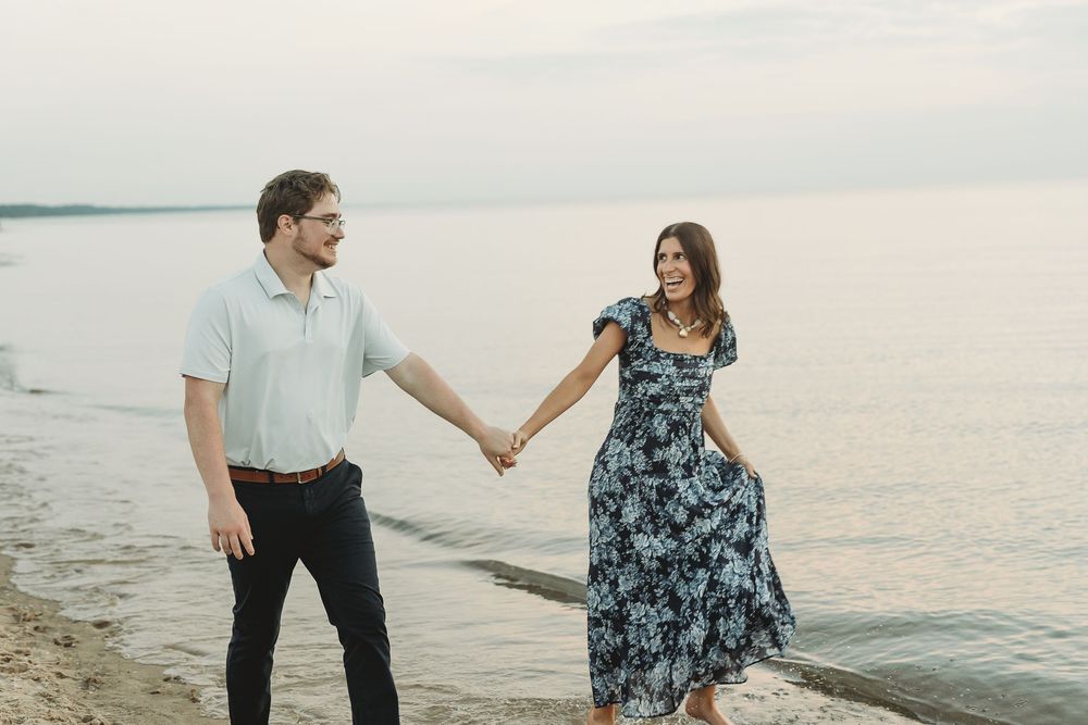 Couple holding hands and smiling at each other on a rocky beach shore at sunset.