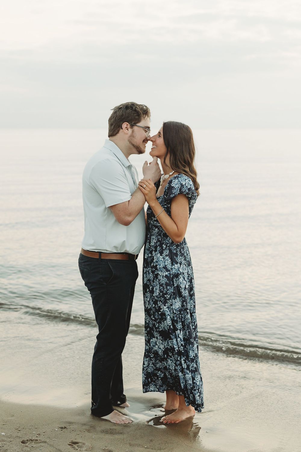 Couple sharing a romantic kiss on a sandy beach shore, man in white shirt and woman in blue floral dress.