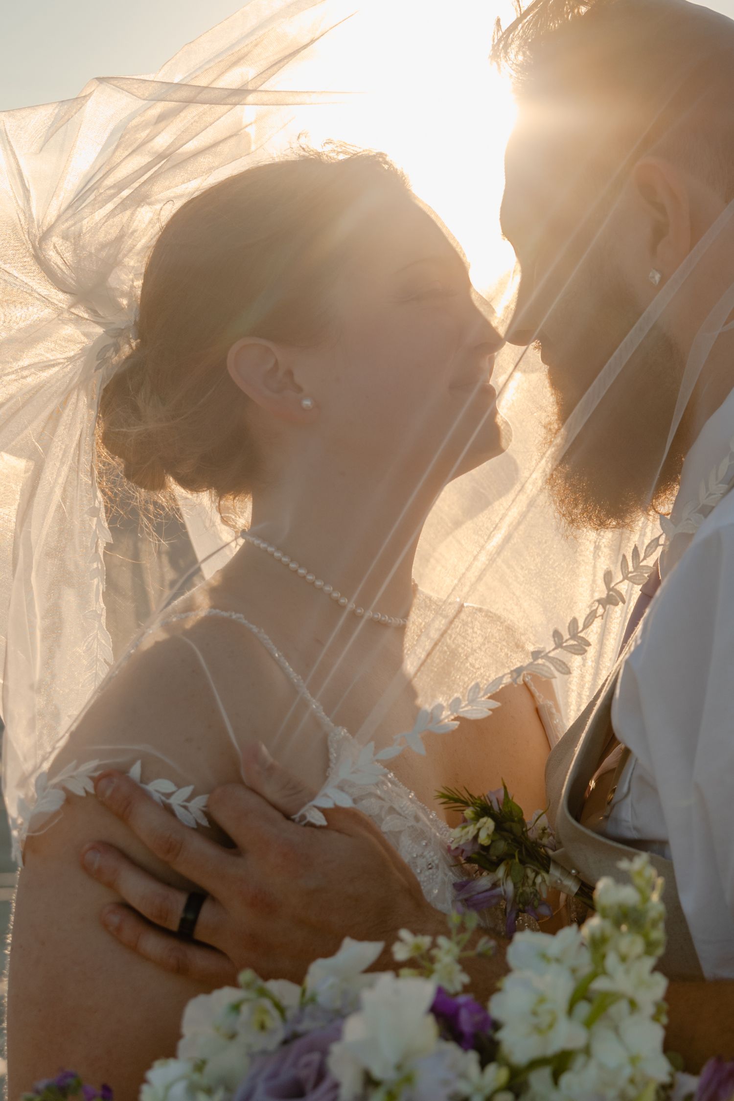 Black and white photo of a bride and groom sitting together on sandy beach dunes in wedding attire.