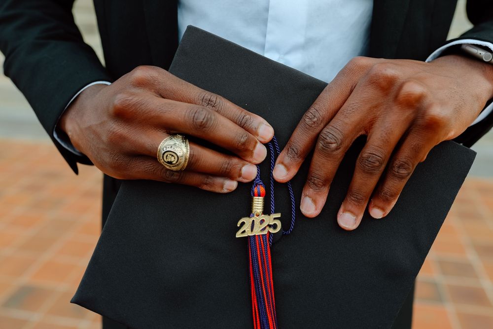 Close-up of graduate hands holding black cap with 2025 tassel and wearing a gold class ring.