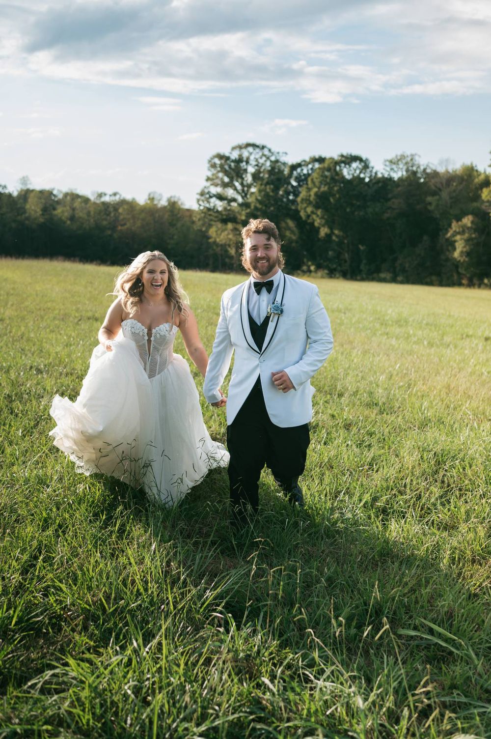 A joyful bride and groom run hand-in-hand through a lush green field on their wedding day.