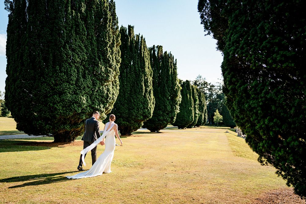 A picturesque garden path lined with tall cypress trees leads through landscaped grounds, creating a scenic walkway.