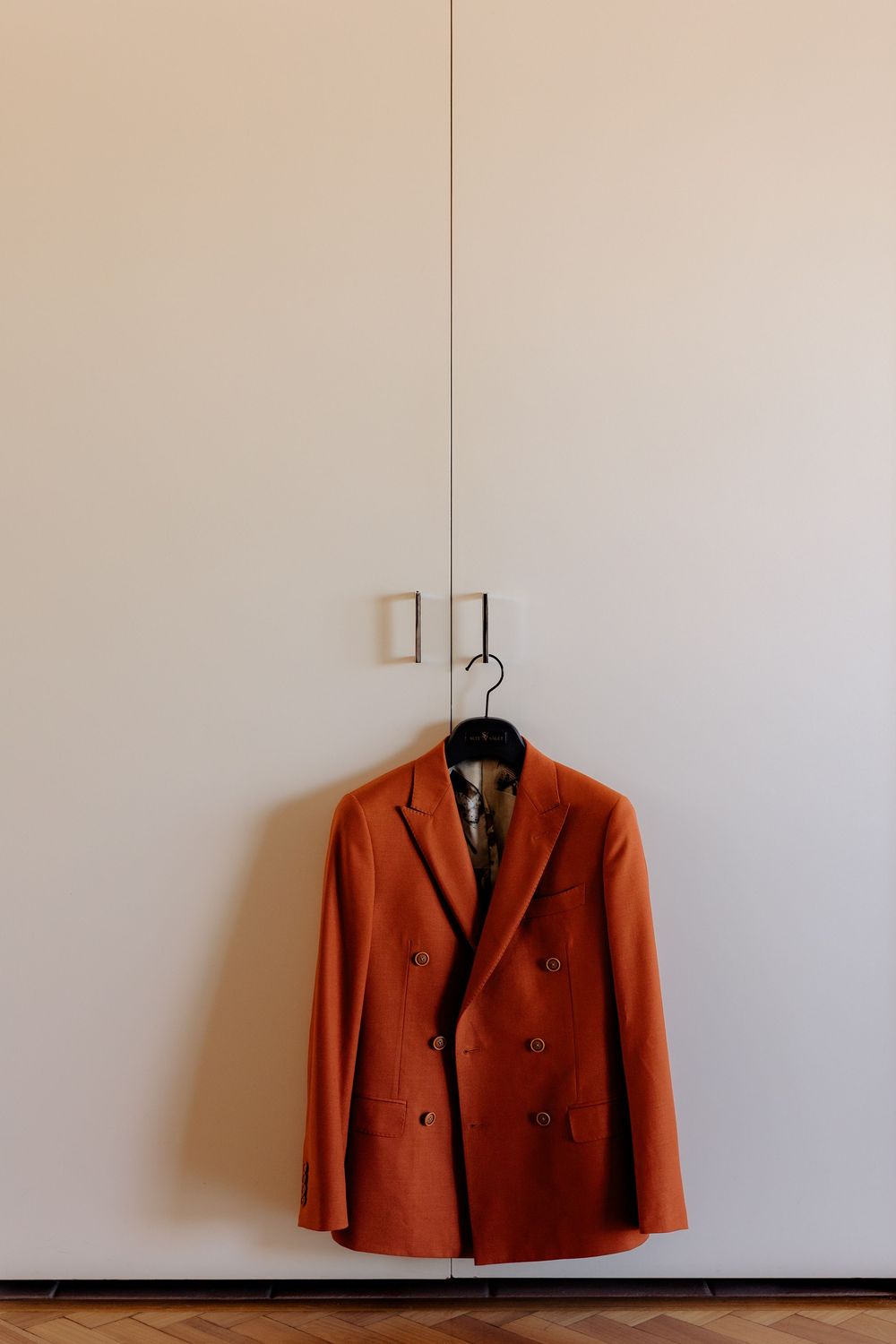 An orange double-breasted blazer hanging on a wall hook against a white background.