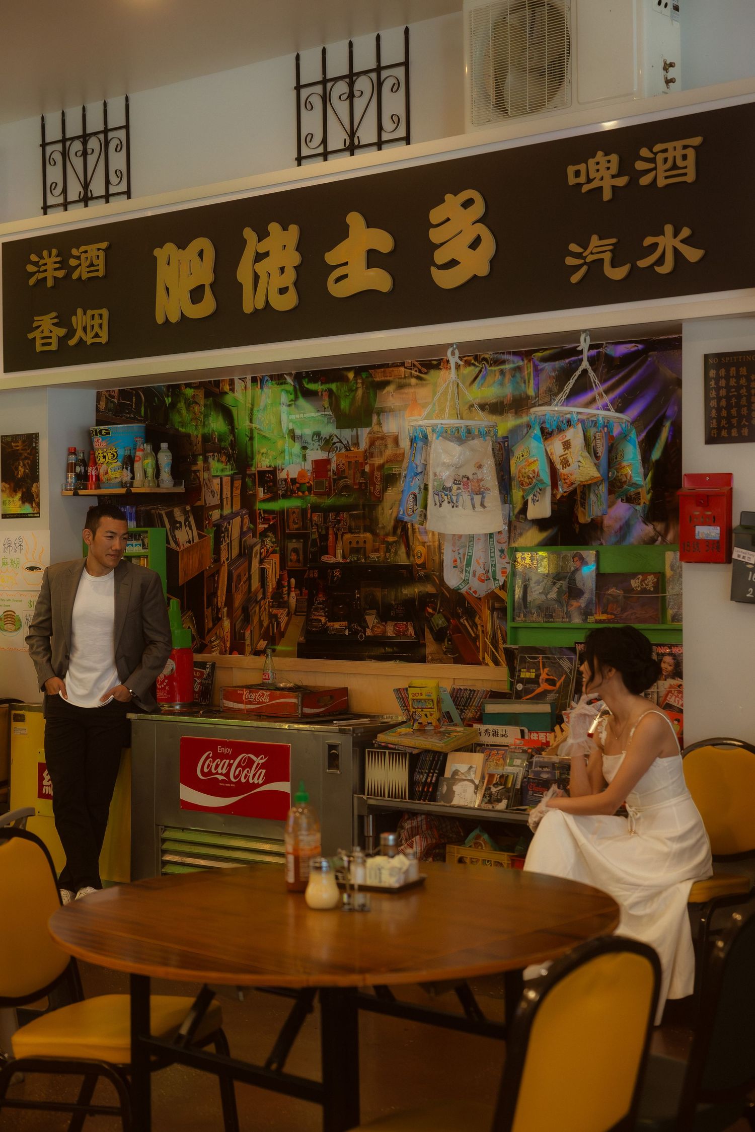 Couple in vintage Hong Kong shop setting with Coca-Cola fridge and Chinese signage for beer and cigarettes.