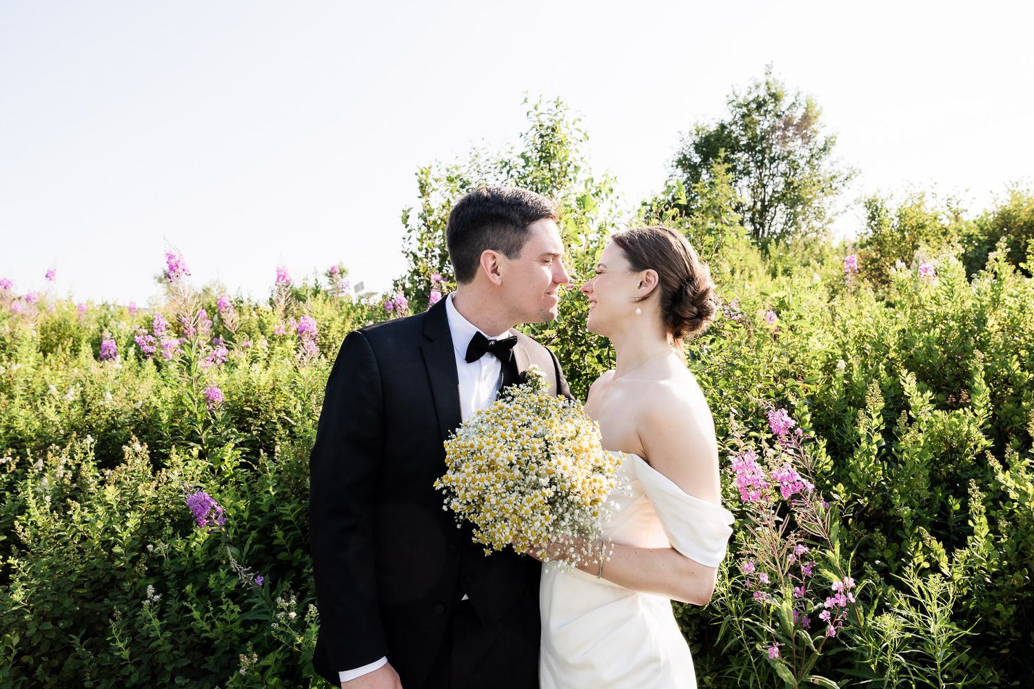 Newlywed couple gazing at each other with love in their eyes, set against a beautiful field of fireweed flowers.