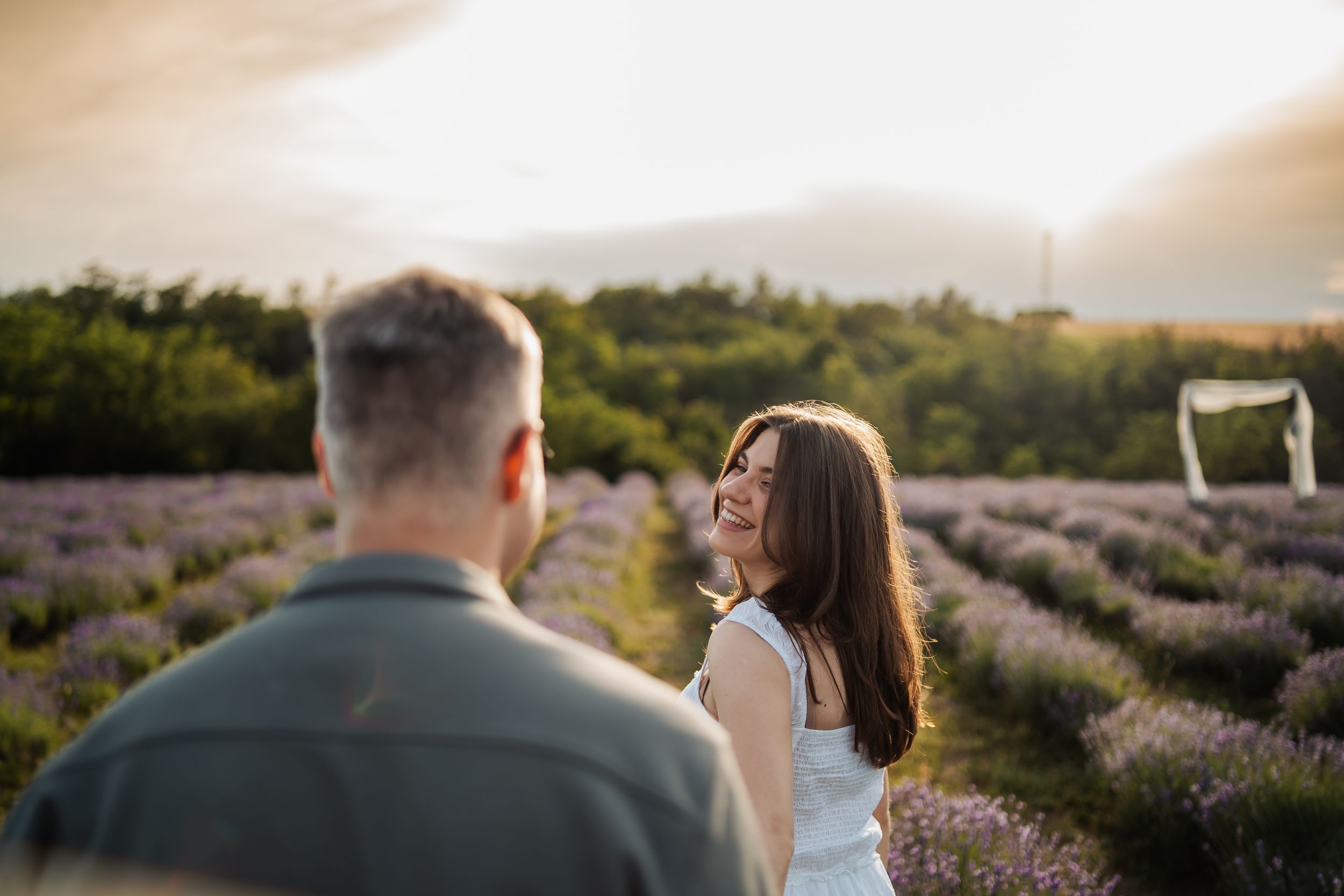 Couple smiling in a lavender field at sunset, woman in white dress laughing joyfully.