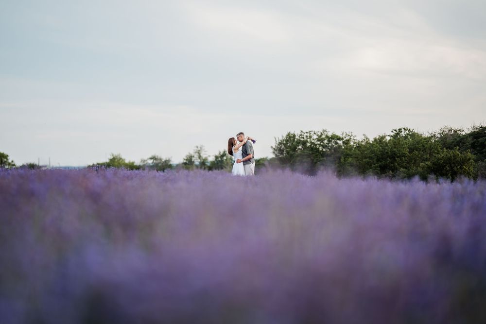Pár ölelkezik egy hatalmas levendulamezőn, melynek lila virágai a horizontig nyúlnak a lágy ég alatt.