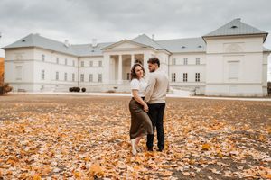 Couple dancing among autumn leaves in front of a grand white mansion on a cloudy fall day.