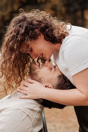 A couple sharing a romantic kiss outdoors, with the woman's curly hair cascading down as they lean close together.