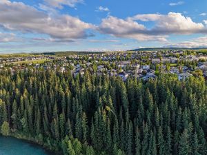 Aerial view of a residential neighborhood surrounded by dense evergreen forest beside a turquoise river under a partly cloudy sky.