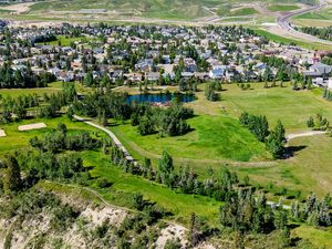 Aerial view of a lush green golf course surrounded by residential neighborhood with a pond and trees in Calgary, Alberta.