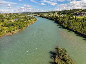 Aerial view of a wide turquoise river winding through lush green trees under a partly cloudy blue sky.