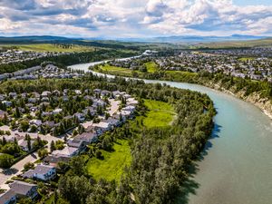 Aerial view of a river winding through a lush Canadian town with green parks, residential homes, and rolling hills.