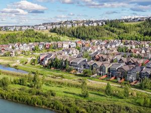 Aerial view of a suburban neighborhood with rows of homes along a river, surrounded by lush green trees and hills.