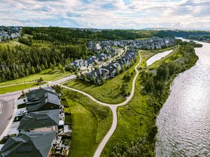 Aerial view of a riverside residential community with winding paths, green spaces, and dense forest in the background.