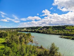 Scenic aerial view of a turquoise river winding through lush green trees under a bright blue sky with white clouds.