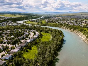 Aerial view of a river winding through a lush green town with residential areas and rolling hills under a cloudy sky.