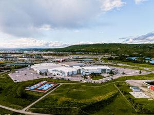 Aerial view of an industrial park with modern buildings, green fields, and a coastal town in the background.