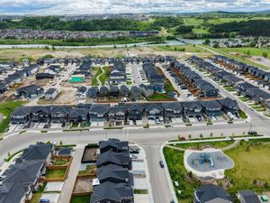 Aerial view of a modern suburban neighborhood with rows of new homes, green spaces, and a playground in a Canadian city.