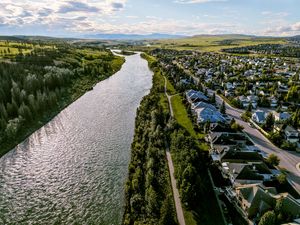Aerial view of a river alongside a residential neighborhood with lush trees and rolling hills in the background.