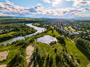Aerial view of a river winding through lush green landscape with residential neighborhoods under a dramatic cloudy sky.