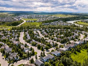 Aerial view of a suburban neighborhood with tree-lined streets, homes, a river, and rolling hills under a cloudy sky.