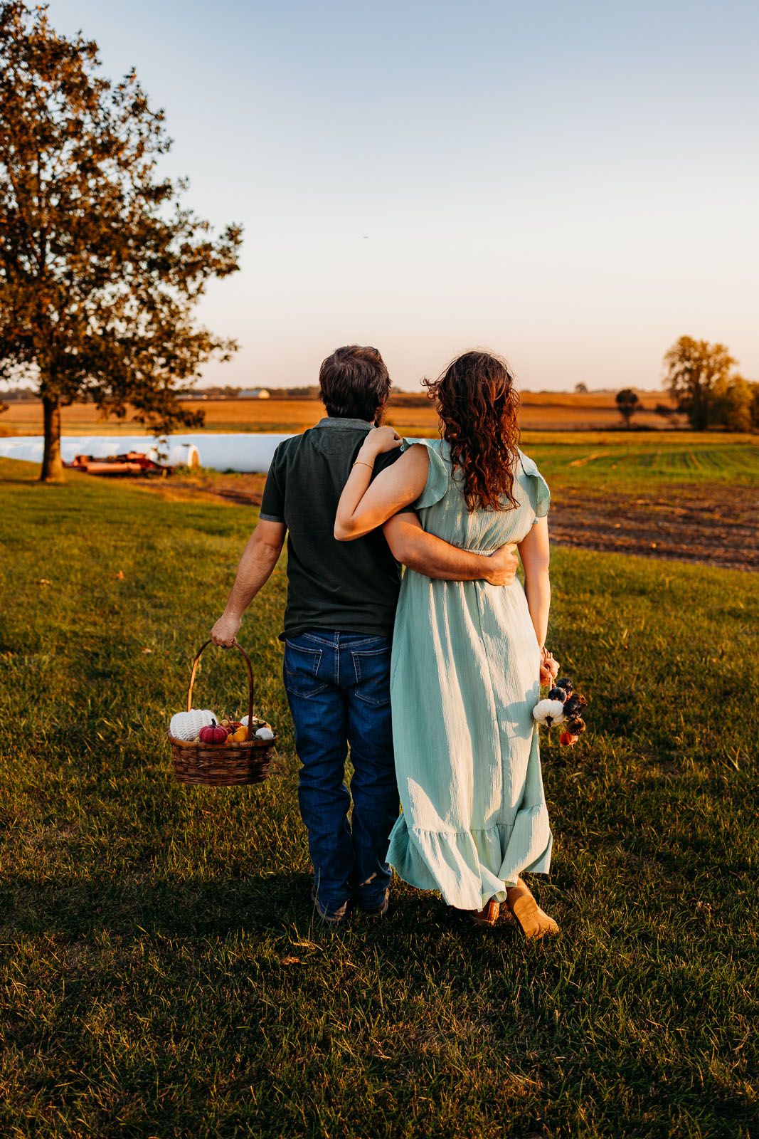 a couple standing together in a field watching the sunset.