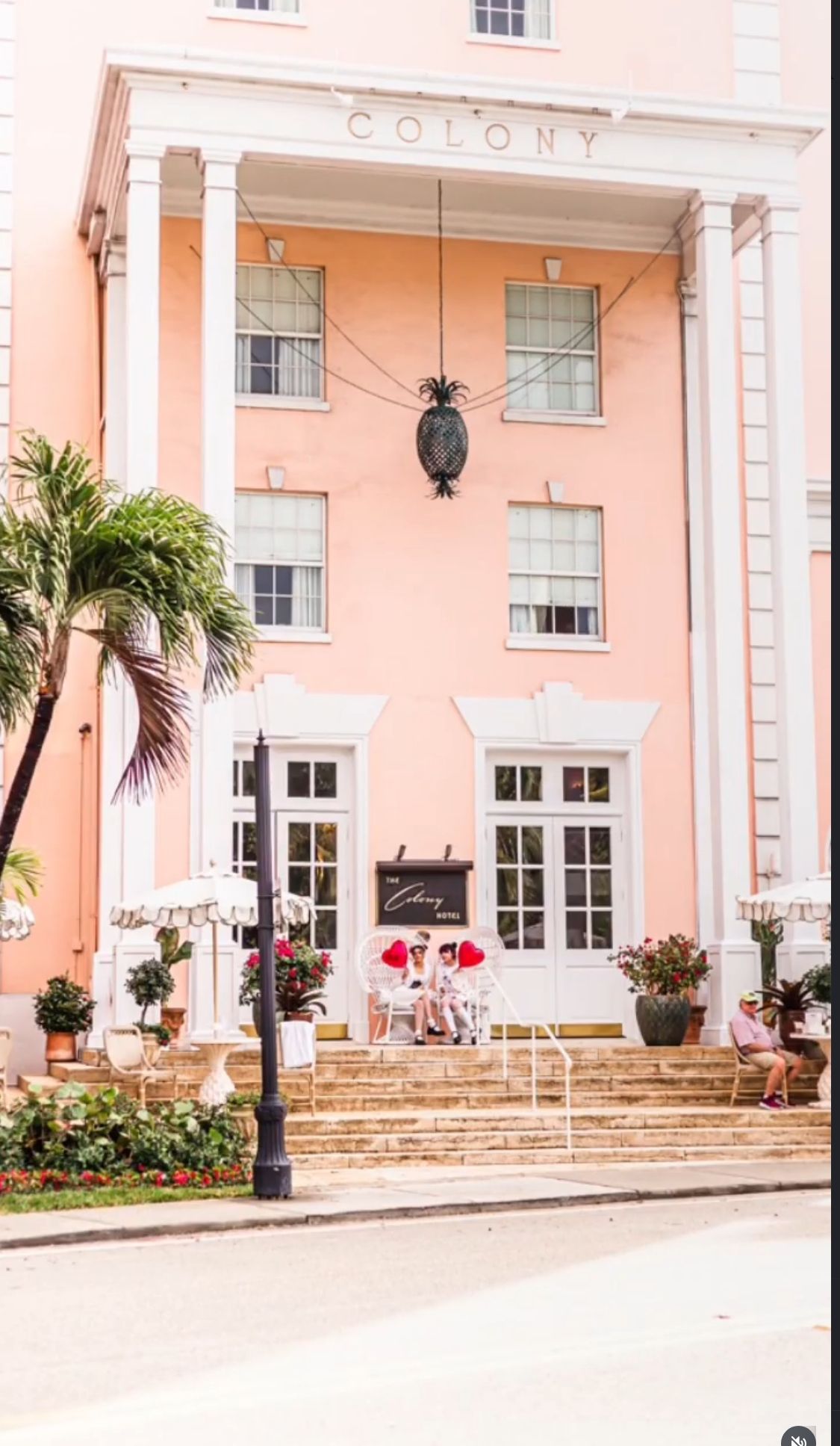 Pink Colony Hotel facade with white columns, palm trees, and outdoor seating on steps in a tropical setting on worth ave palm beach fl.
