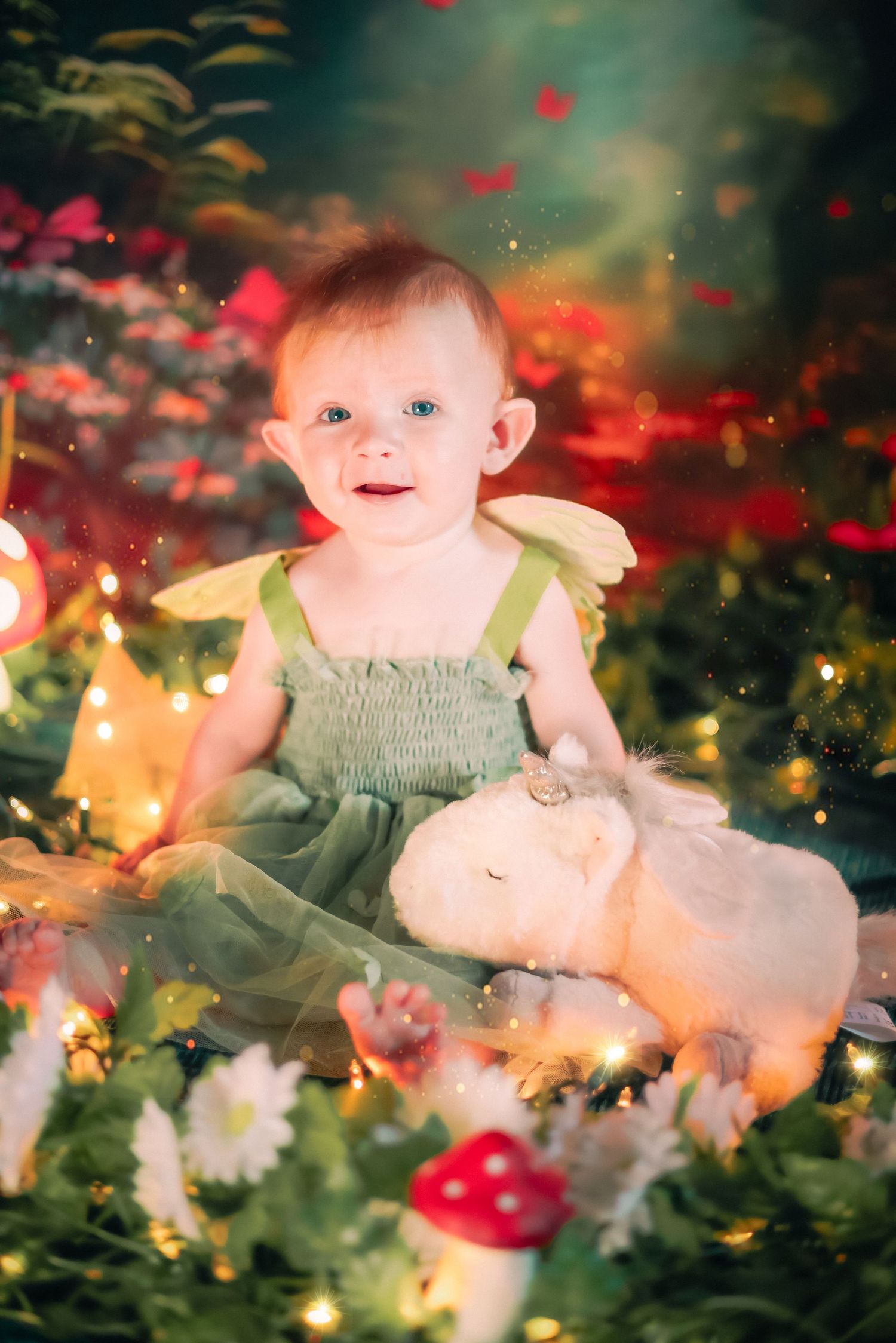 Baby girl in green fairy dress sits with white bunny plush amid flowers, mushrooms, and fairy lights in enchanted garden a home session.