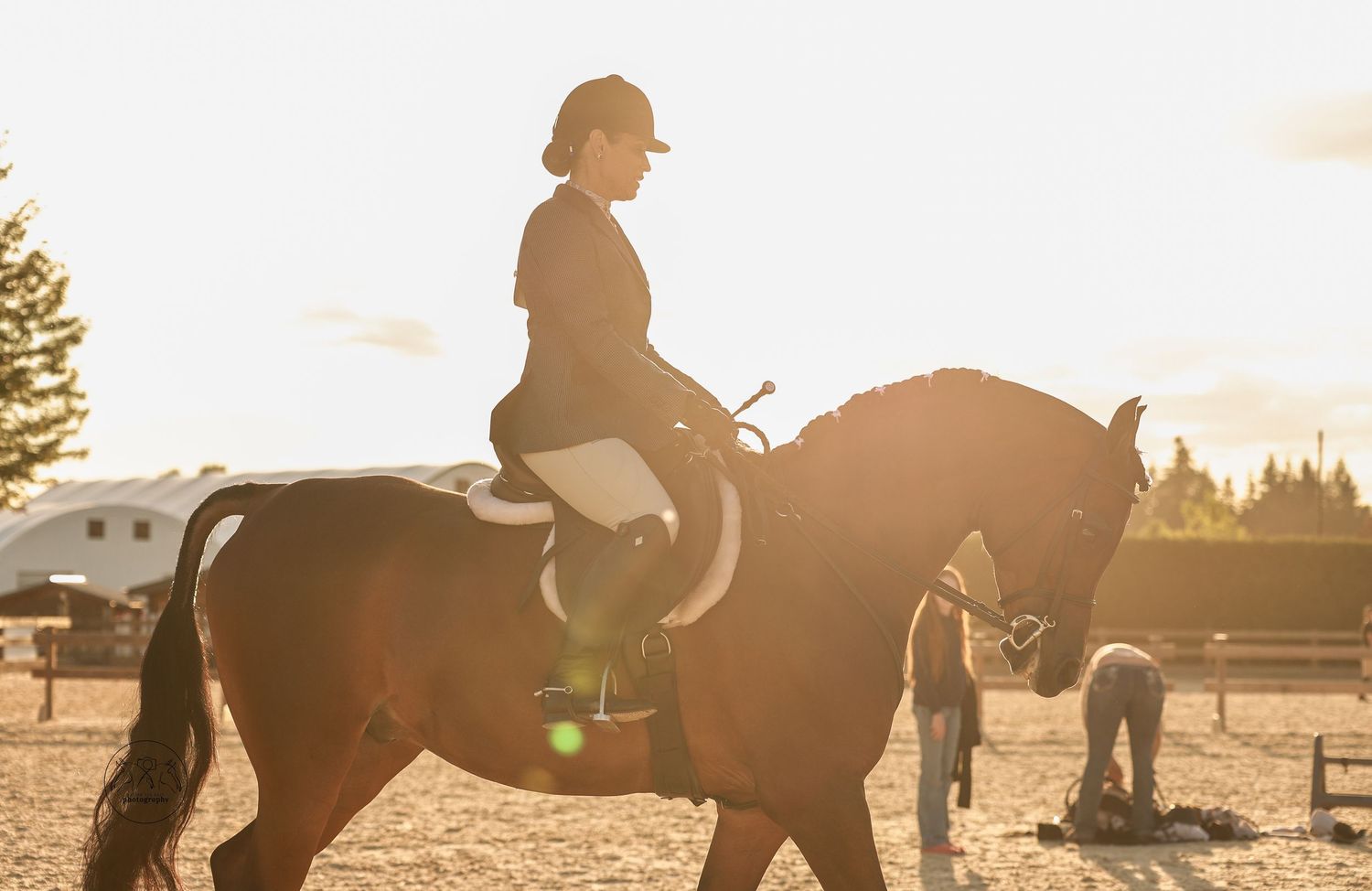 A rider on a chestnut horse during a golden sunset at an outdoor equestrian arena.