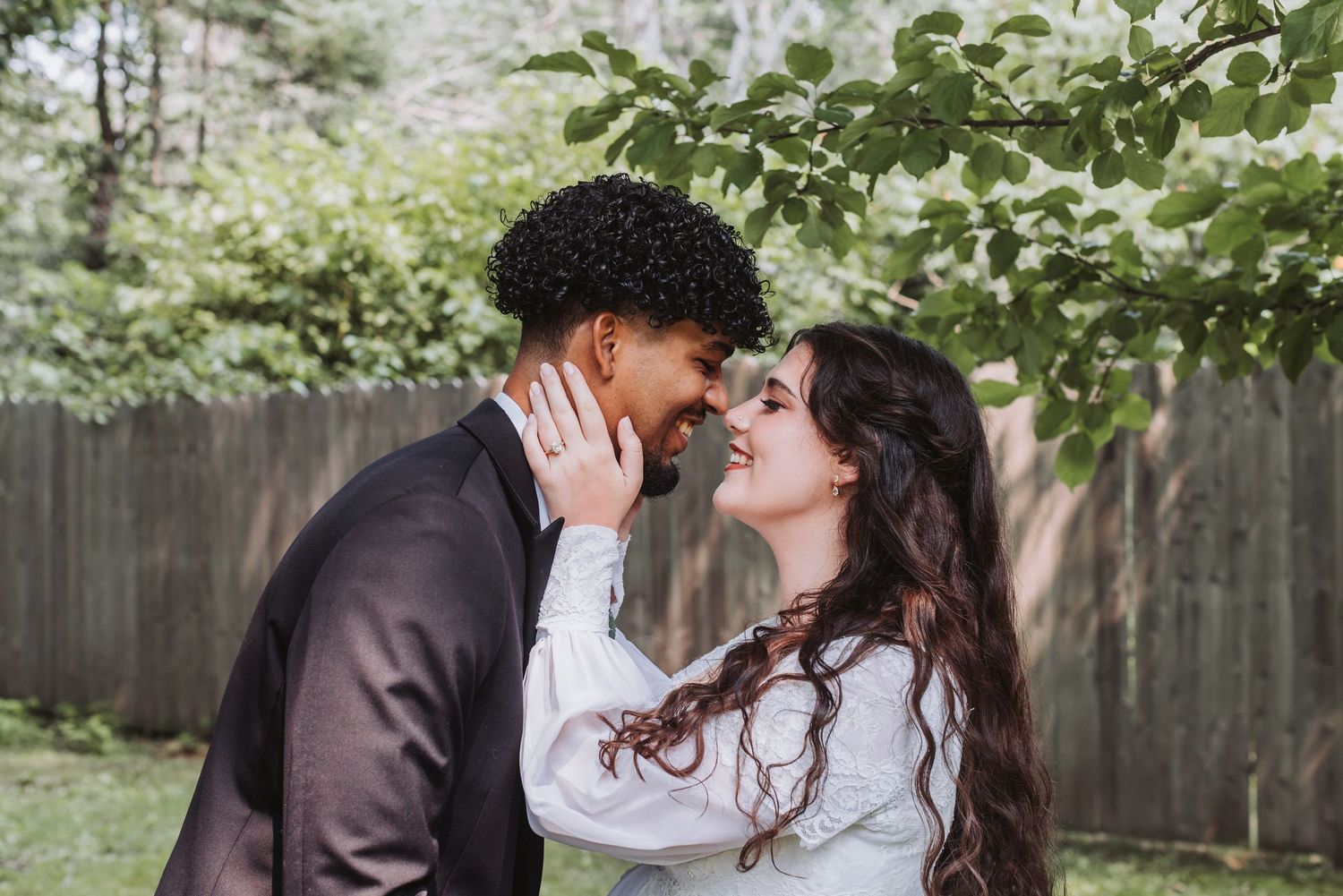 A romantic interracial couple sharing a tender moment, nearly kissing outdoors with lush green trees in the background.