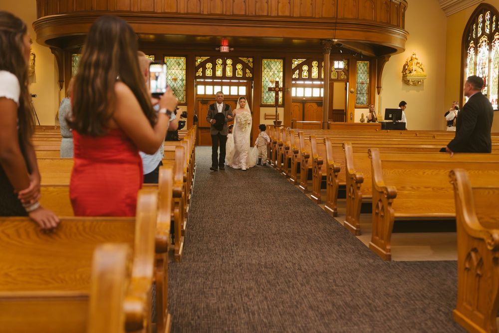 Guests stand in church pews watching a wedding ceremony at the altar of a traditional wooden church.