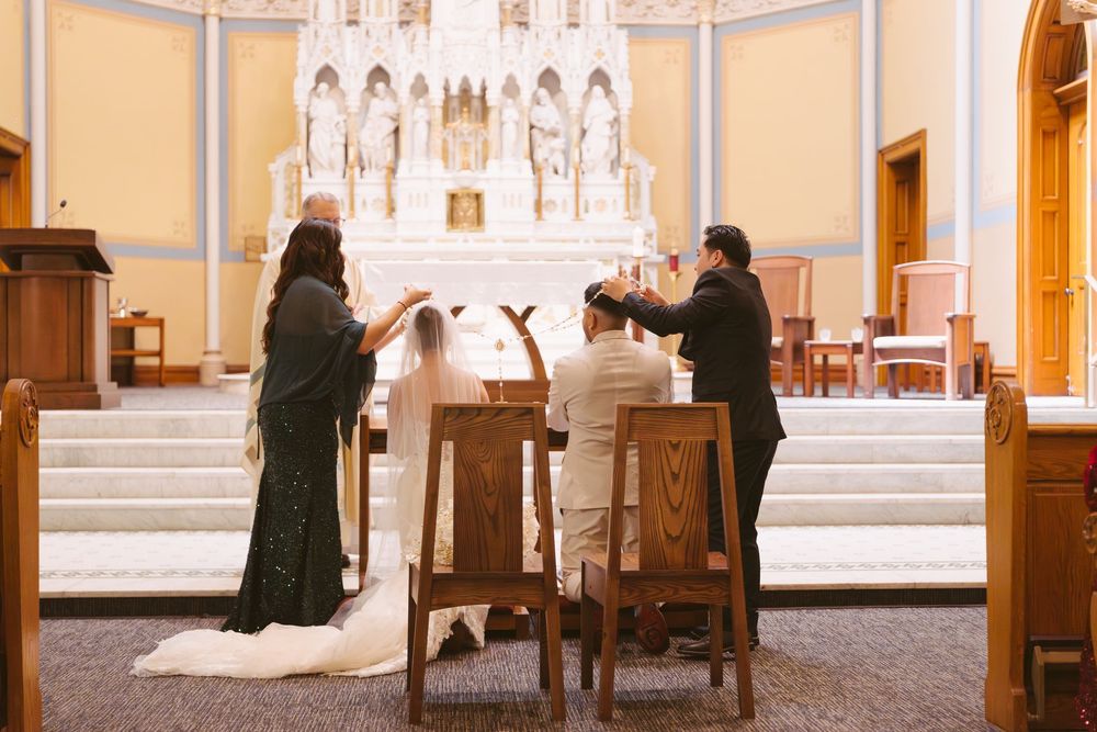 Bride and groom kneel at altar during intimate Catholic wedding ceremony with officiant in ornate church.