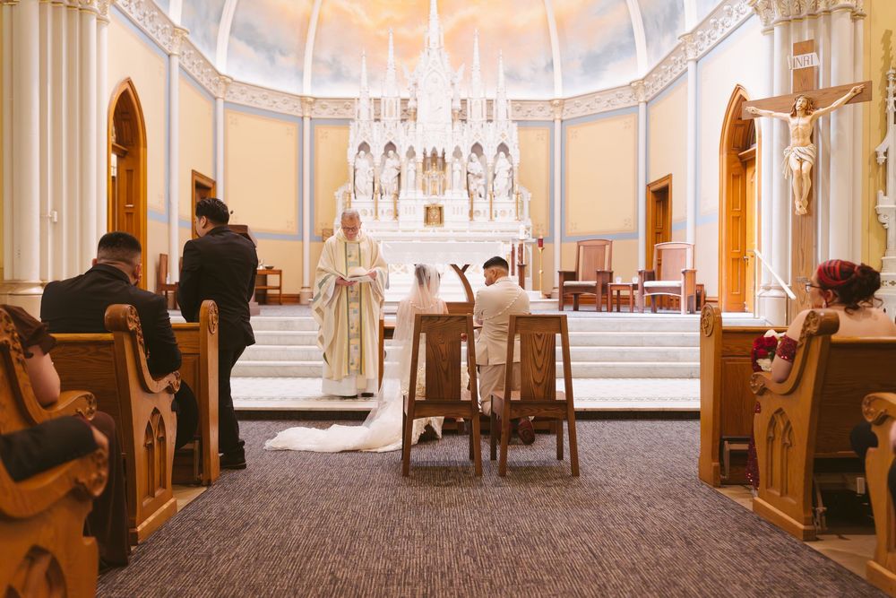 Bride and groom kneel before a priest at the altar during a Catholic wedding ceremony.