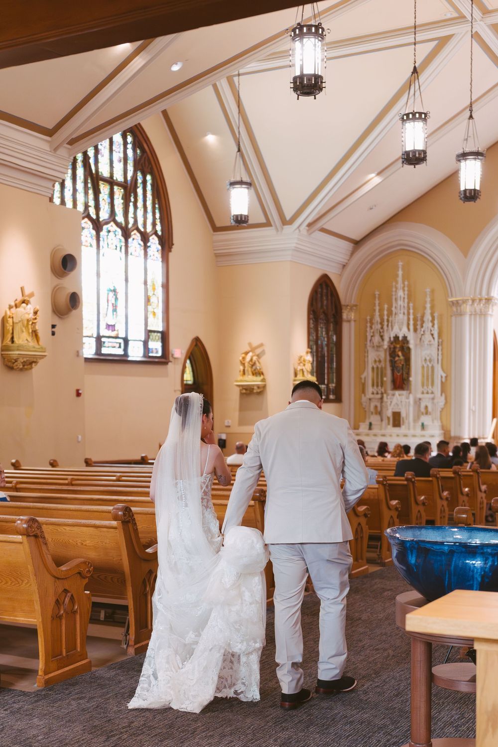 Bride and groom walking down the aisle of an elegant church with stained glass windows during wedding ceremony.