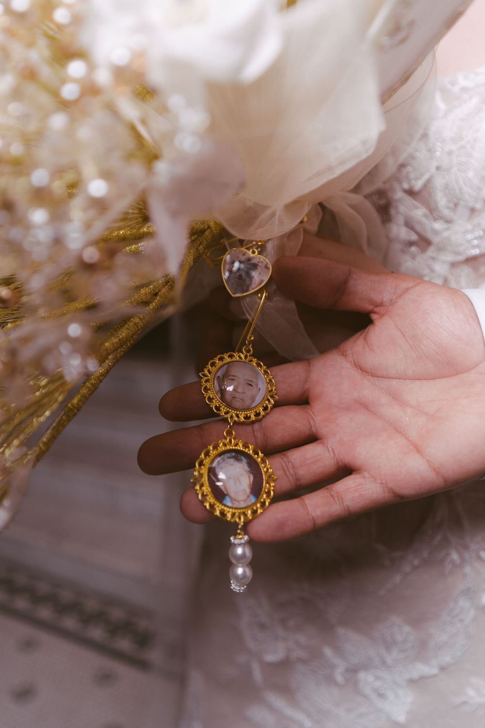 Gold earrings with pink gemstones and pearl drops displayed on a bride's palm near her wedding bouquet.