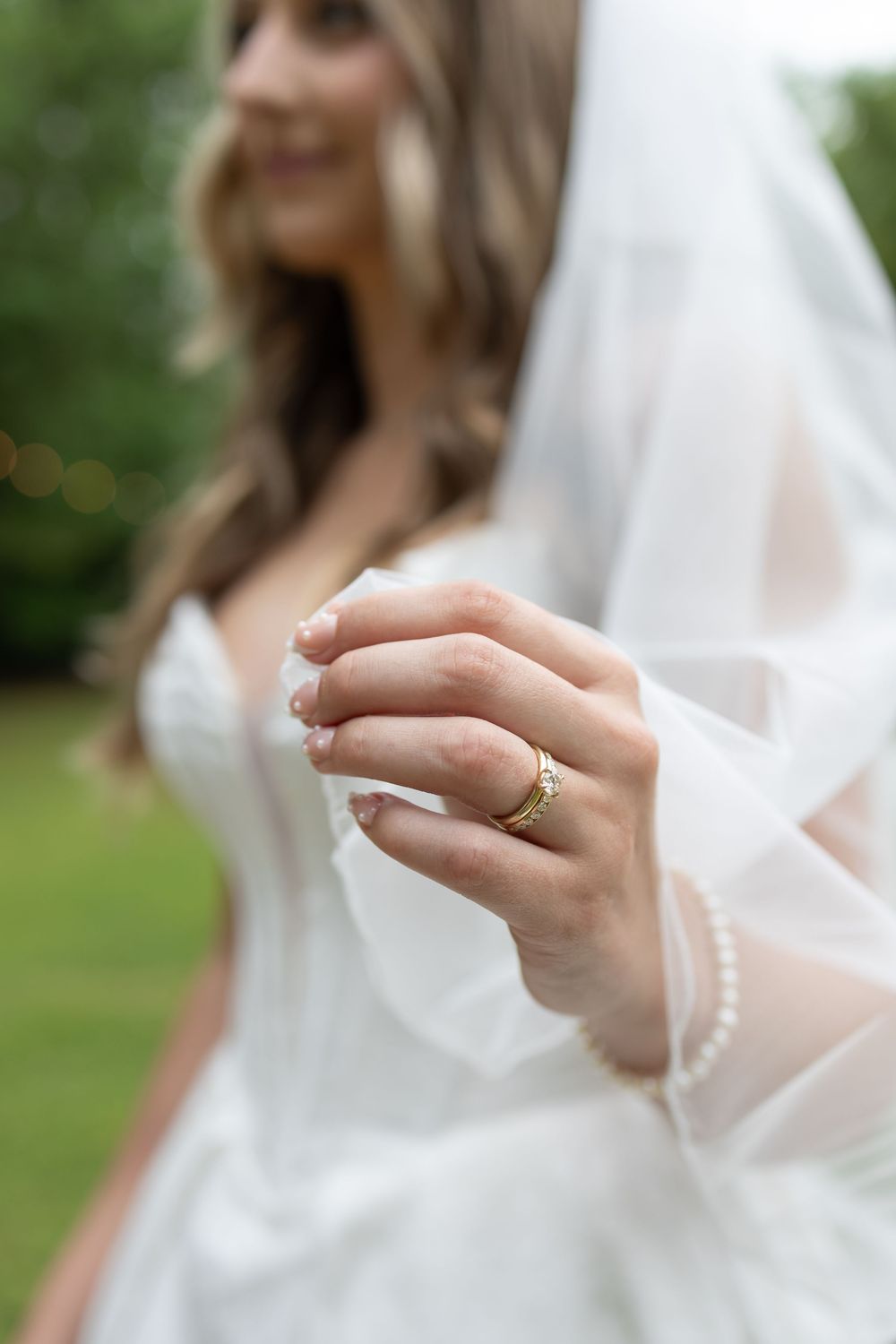 Bride in white gown holding veil, showcasing gold wedding band with intricate design on ring finger.