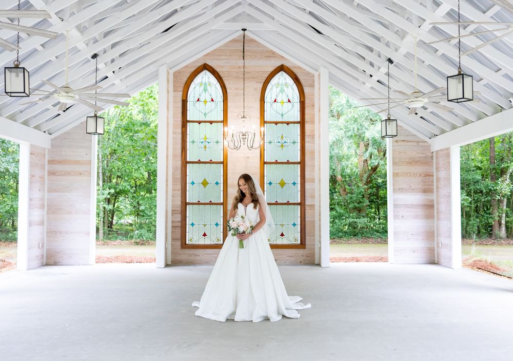Bride in white gown stands in elegant open-air chapel with stained glass windows and hanging lanterns.
