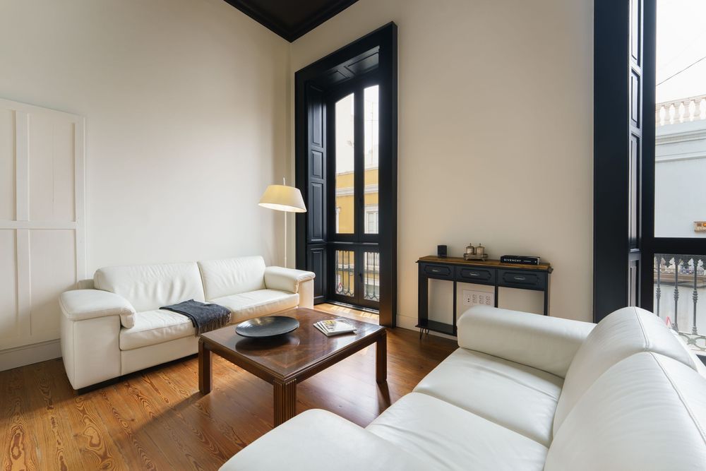 Bright living room with white sofas, wooden coffee table, hardwood floors, and elegant black French doors.