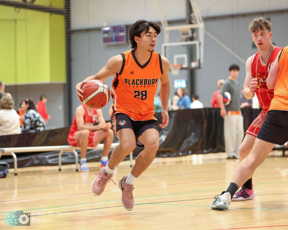 Blackburn player #28 drives to the basket during an indoor basketball game wearing an orange jersey.