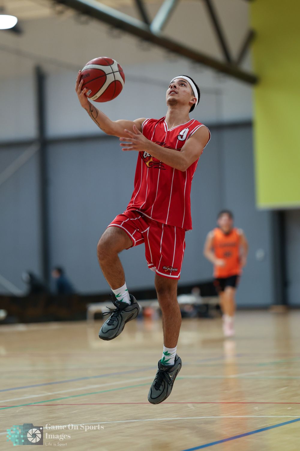 Basketball player in red uniform leaps for a layup shot during an indoor game.