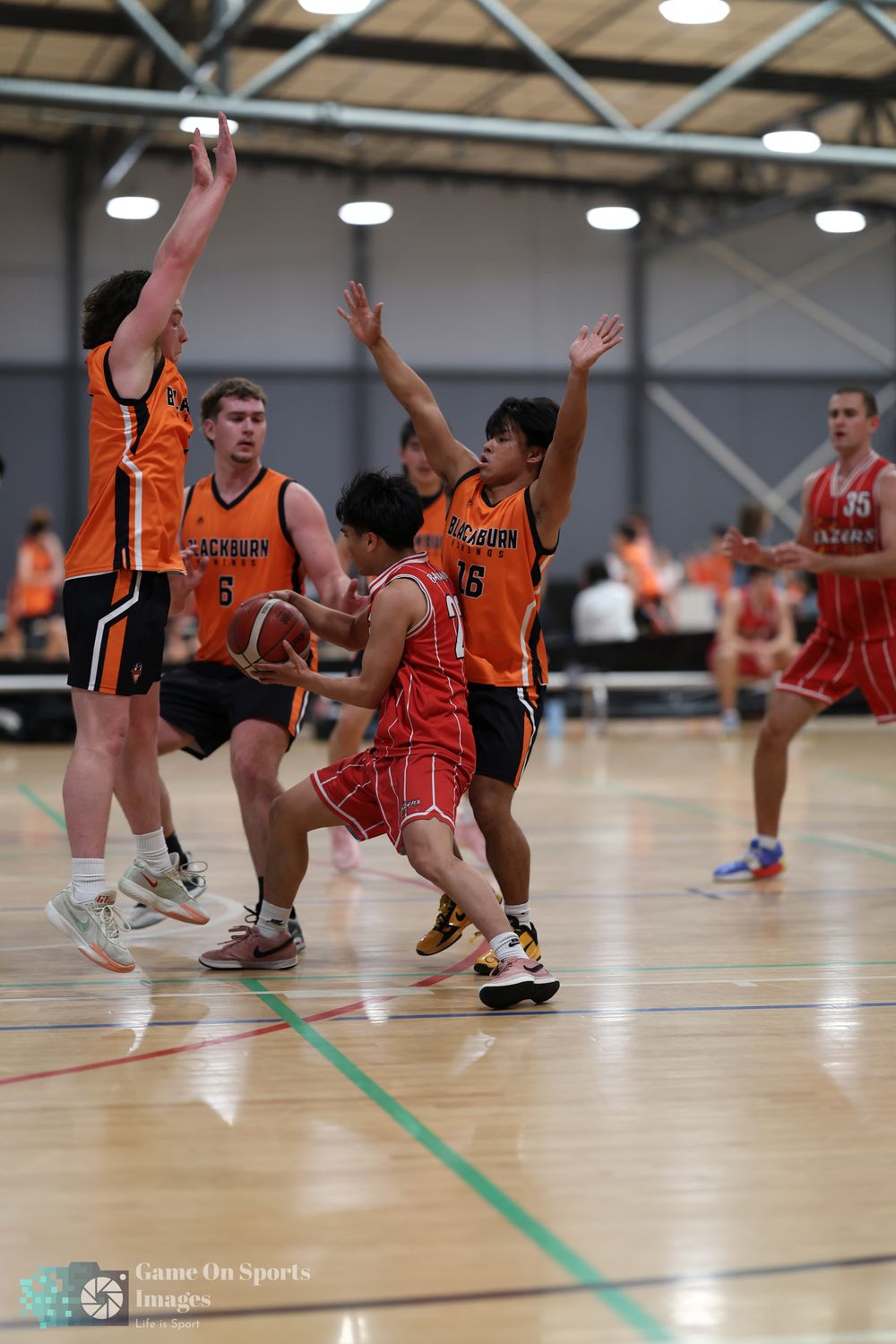 Basketball players in orange Blackburn uniforms defend against a red-uniformed player driving to the basket indoors.