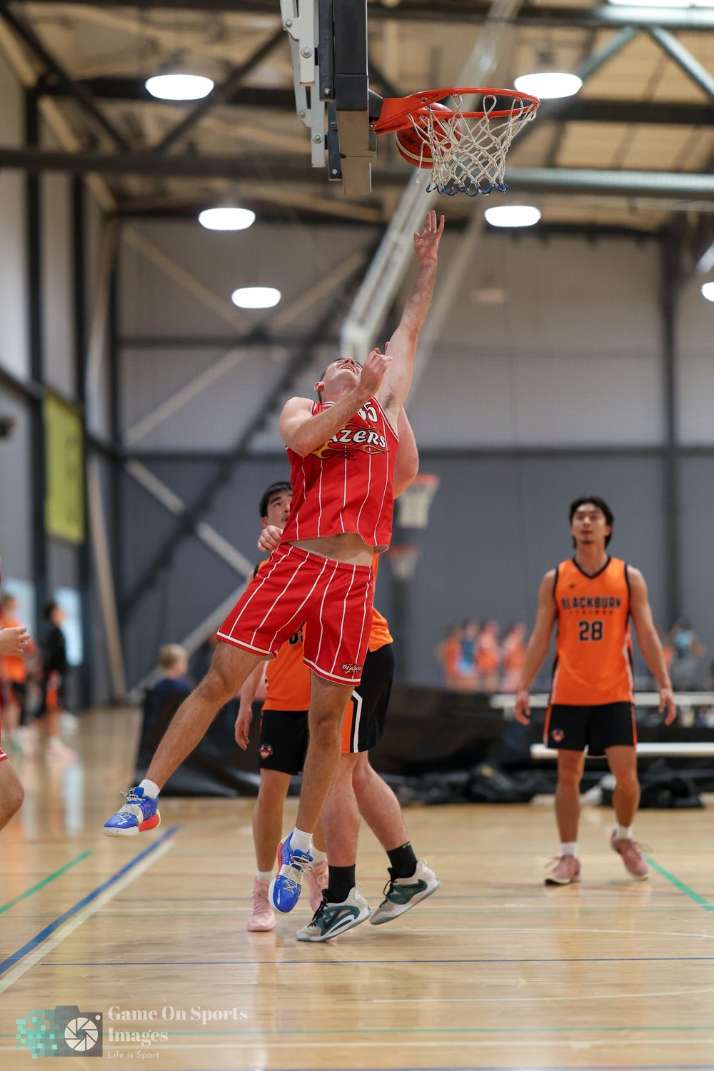 Basketball player in red uniform attempts a layup during an indoor game against opponents in orange jerseys.