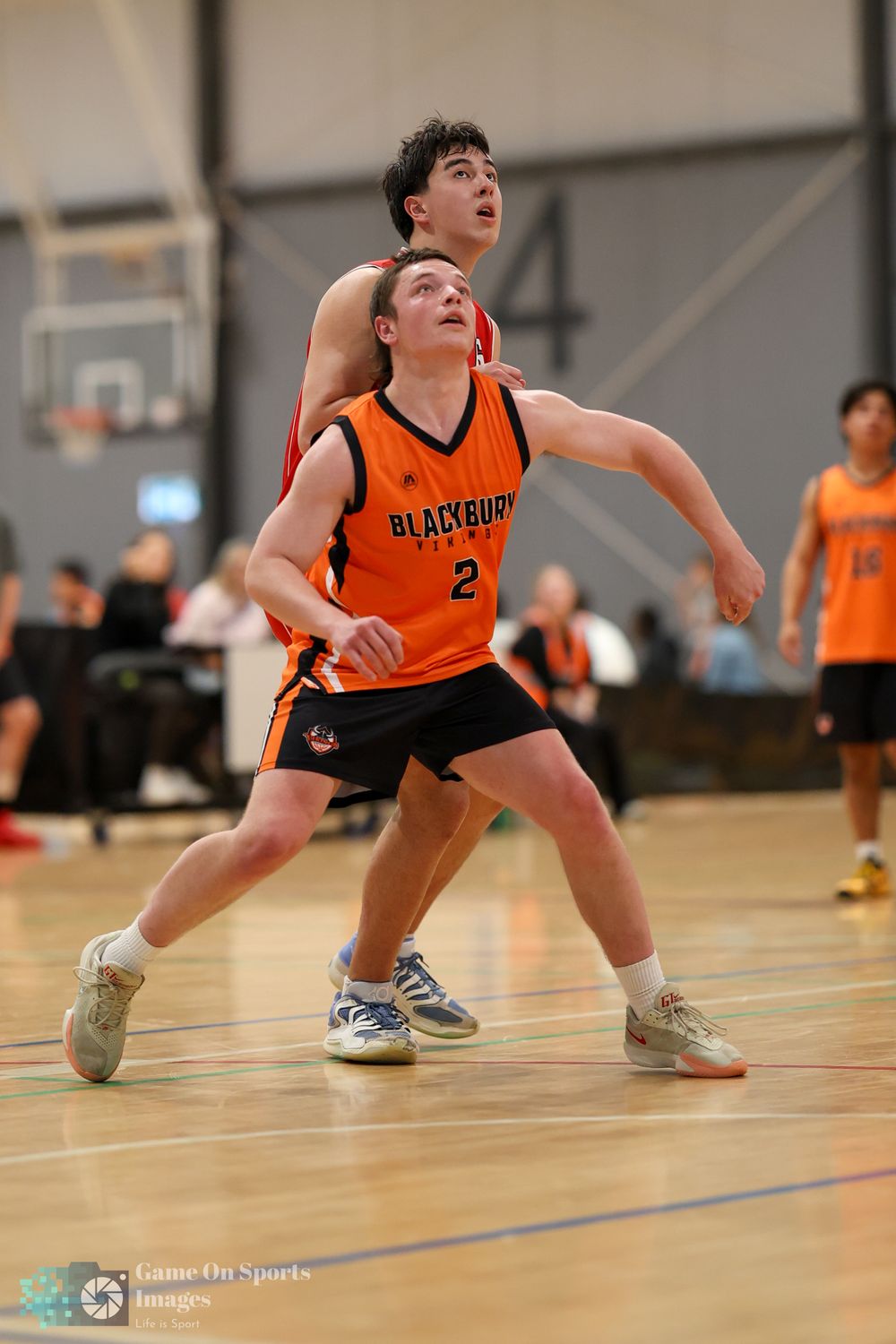 Two youth basketball players in orange Blackburn uniforms compete for position on an indoor court during a game.
