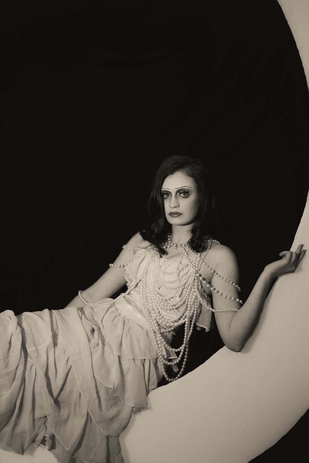 Black and white portrait of a woman in pearl necklaces and white dress seated in circular frame.