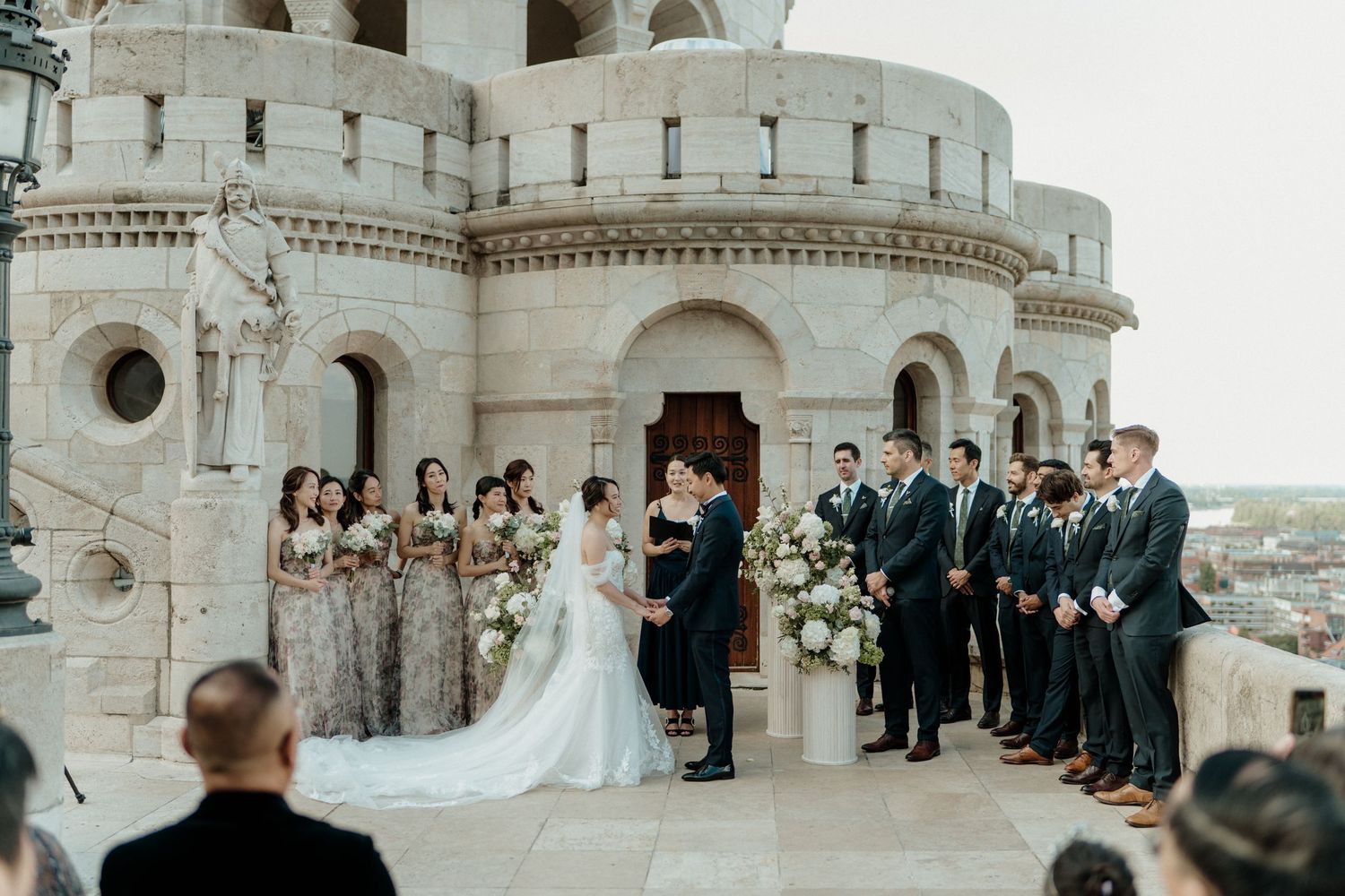 Outdoor wedding ceremony at Fisherman's Bastion Budapest with bride, groom, bridesmaids in silver gowns and groomsmen in dark suits.